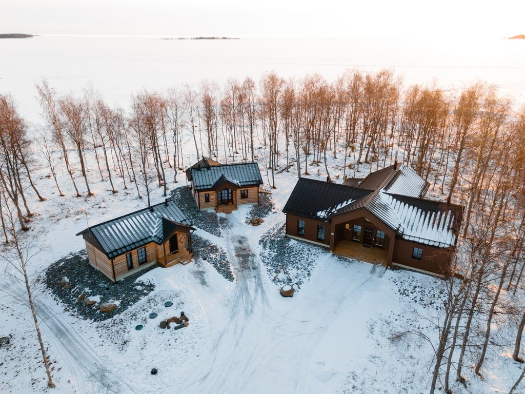 Aerial view of three cabins on a snowy shore by the frozen sea