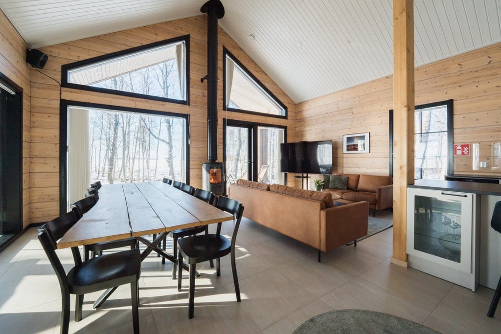 Long dining table, leather sofas and a stove by tall windows