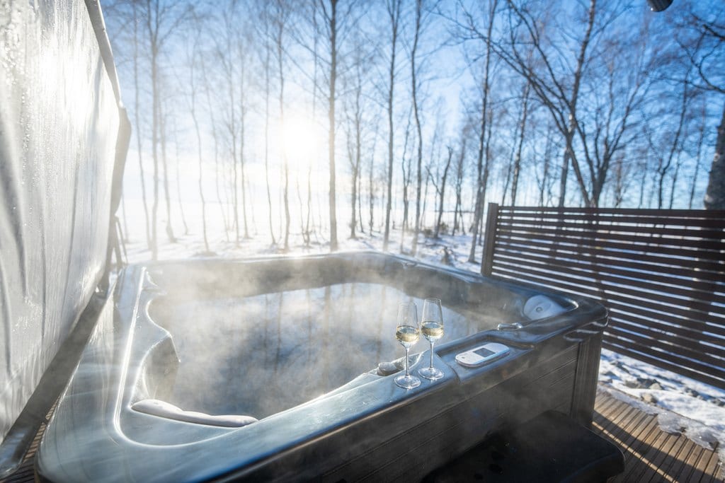Steaming hot tub with two glasses in winter sunshine