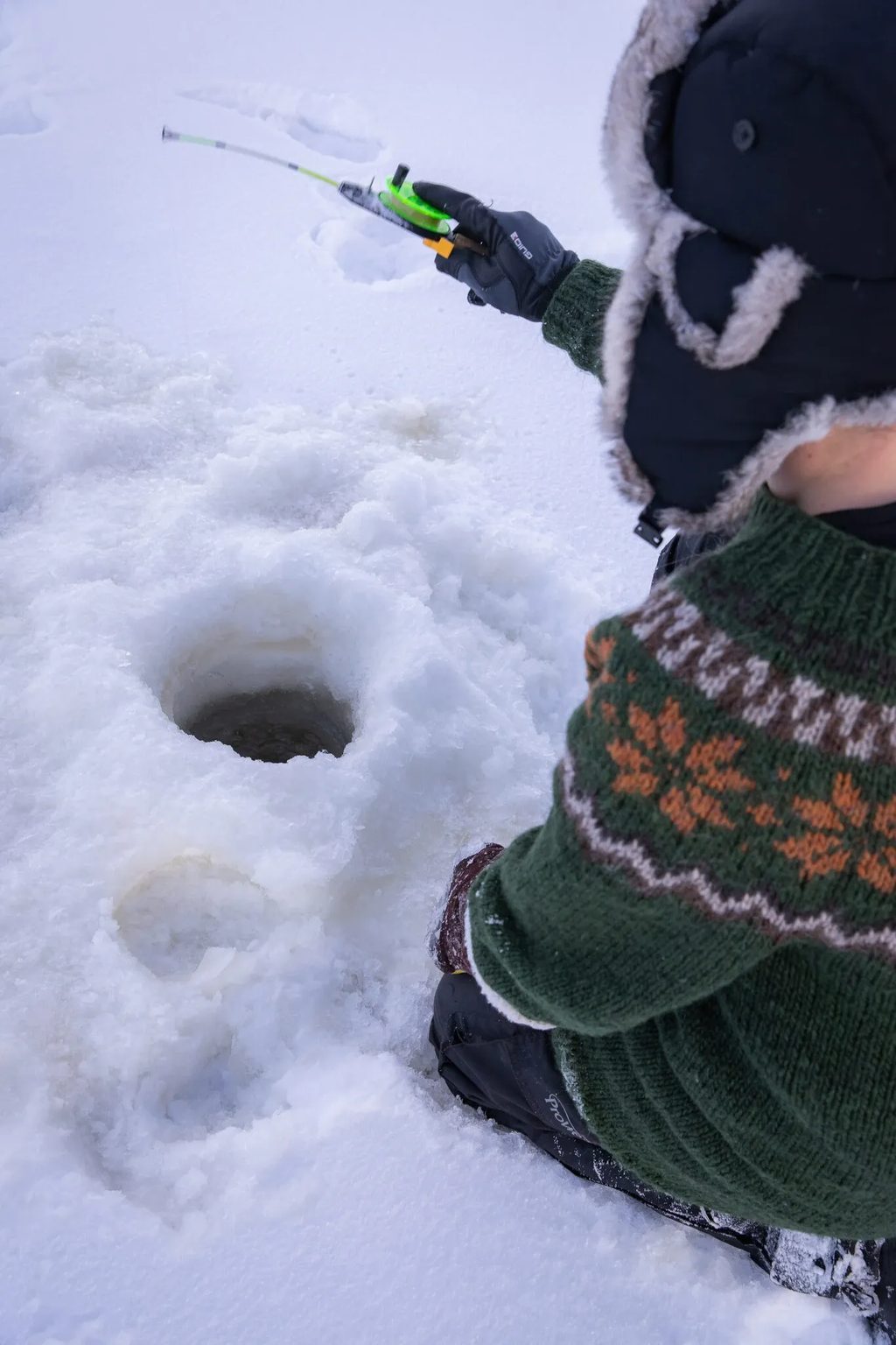 An ice fisher by a hole in the snowy ice