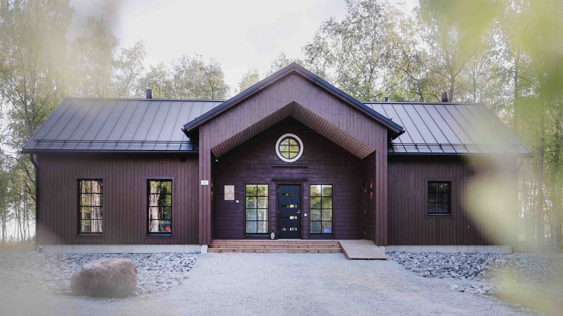 Aava dark brown main building with a gravel yard in front