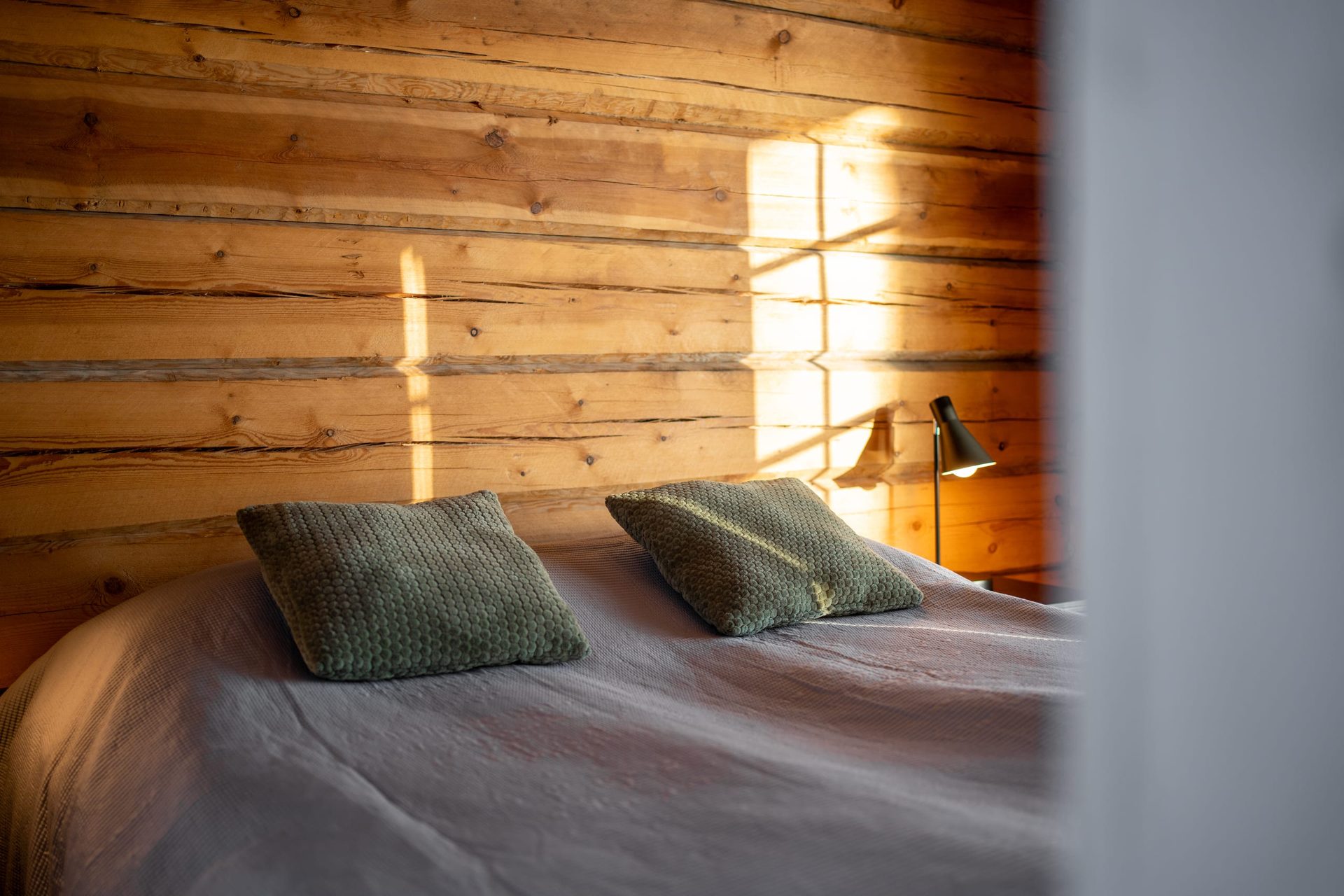 Uitto bed with green pillows against a log wall
