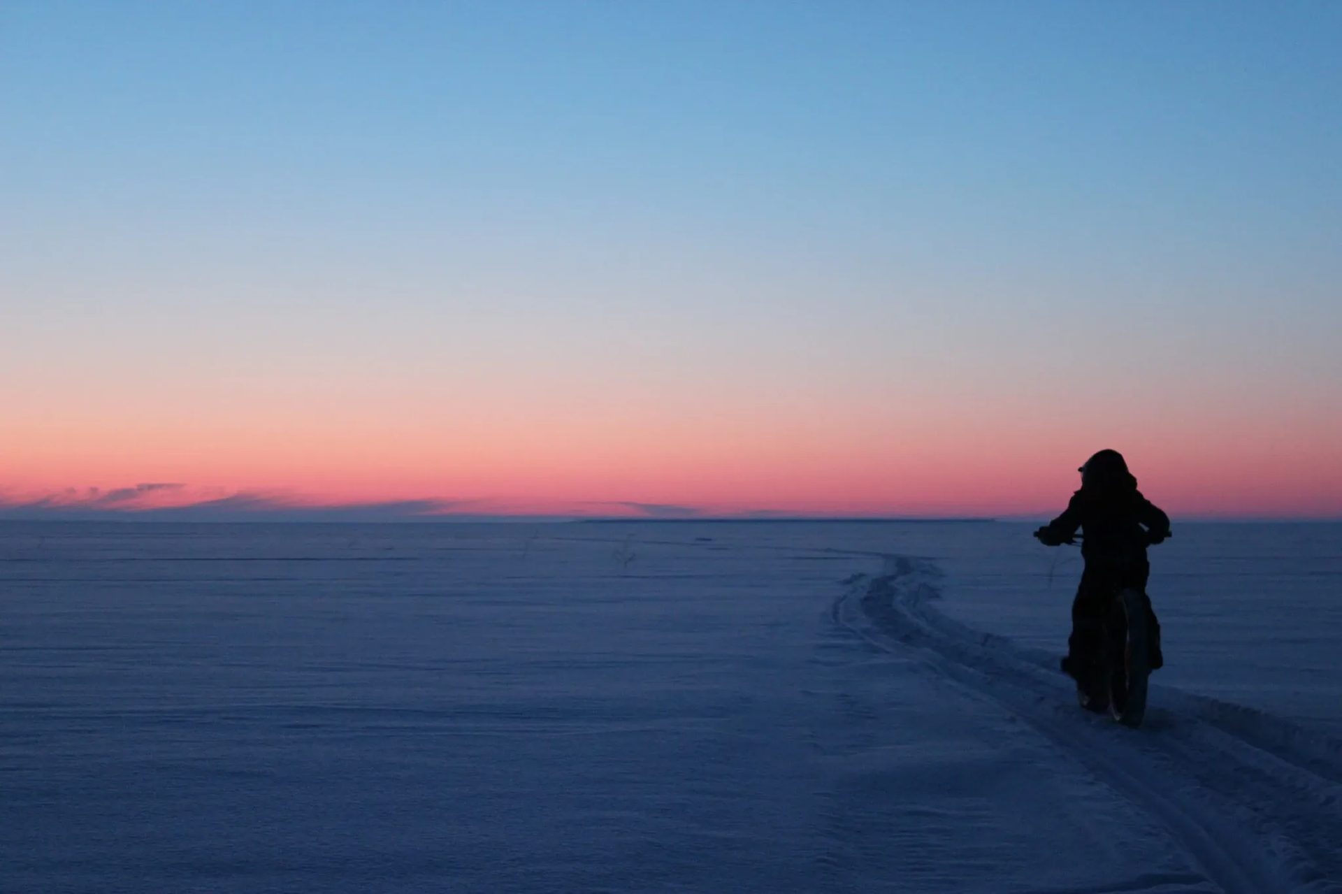 A person walking on the snowy sea ice at dusk