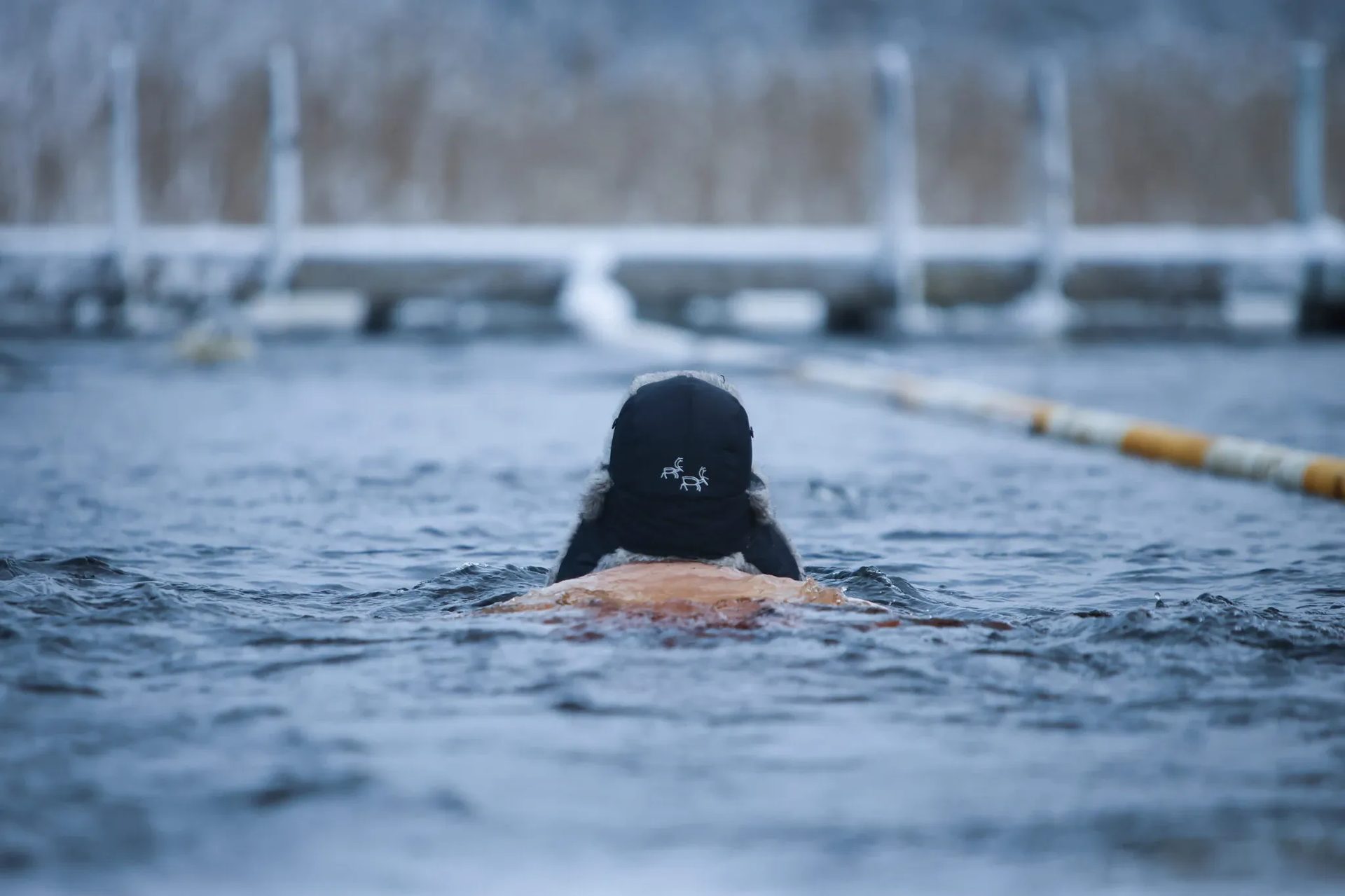A swimmer in an ice hole wearing a hat