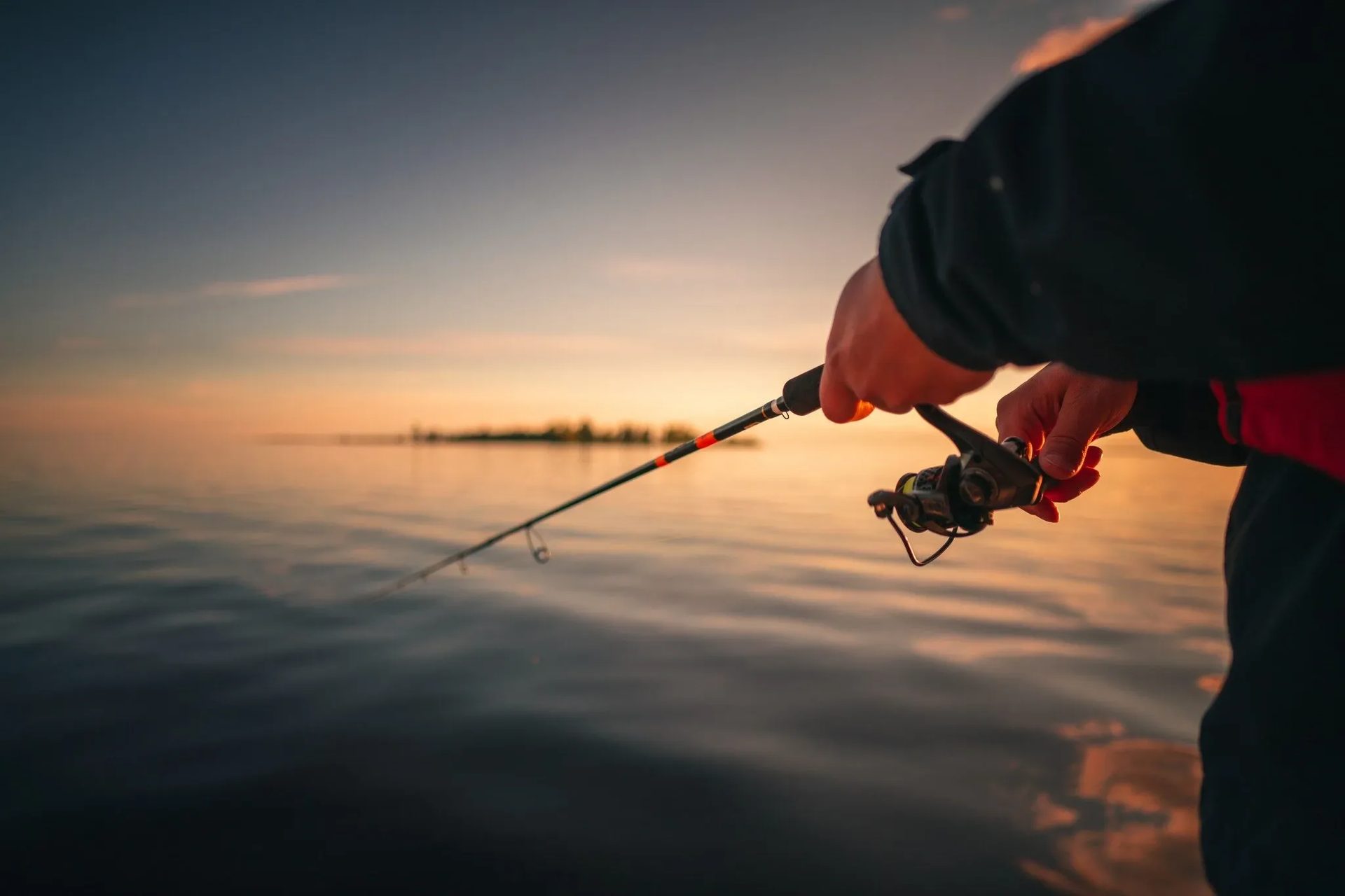 An angler casting on a calm sea at sunset