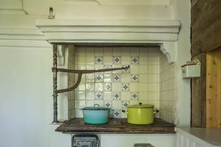 Old wood stove against a tiled wall with two enamel pots