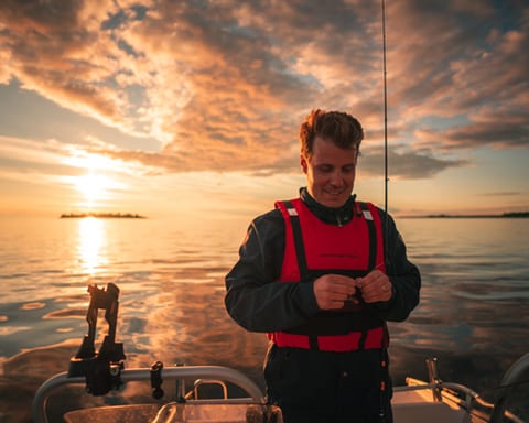 Man in a life vest rigging a fishing line on a boat at sunset