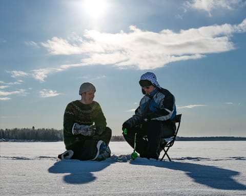 Two people ice fishing in the sunshine