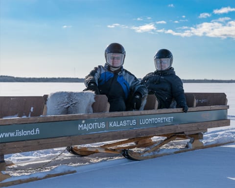 Two passengers in helmets on a sled on the ice