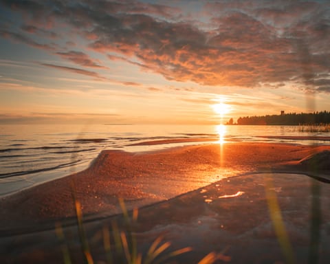 Auringonlasku merenrannan hiekalla ja punertavat pilvet