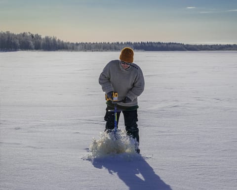 Person drilling a hole in the ice with an auger