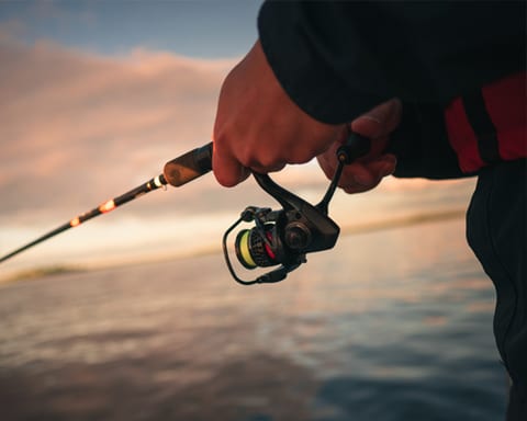 Hand on a fishing rod reel by the water