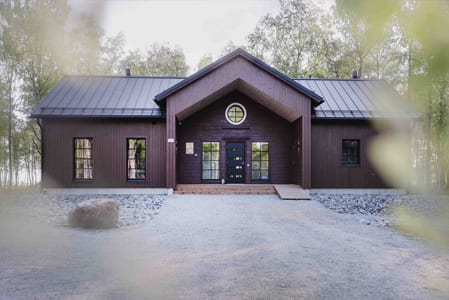Dark wooden cabin with a round window at the end of a gravel path